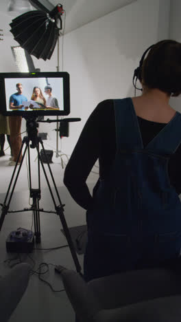 Vertical-Video-Of-Actors-With-Scripts-In-Rehearsal-With-Female-Film-Director-Shooting-Movie-Or-Video-In-Studio-With-Film-Crew-And-Watching-On-Monitor